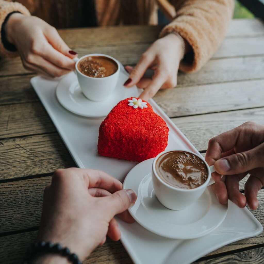 Man och kvinna på dejt i café med kaffe och en hjärtformad bakelse i röd färg Man och kvinna på dejt i café med kaffe och en hjärtformad bakelse i röd färg