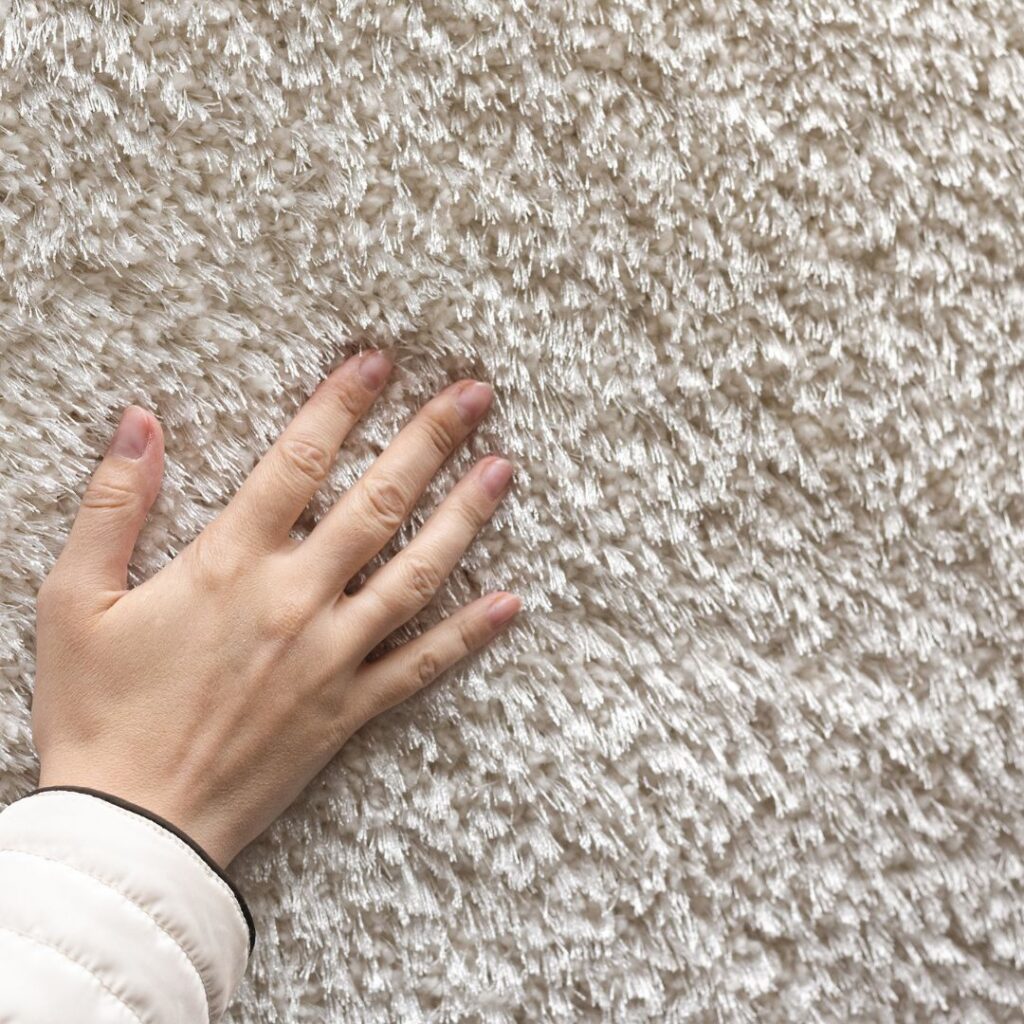 En persons hand smeker den nya mattan som precis placerats i rummets inredning En persons hand smeker den nya mattan som precis placerats i rummets inredning.